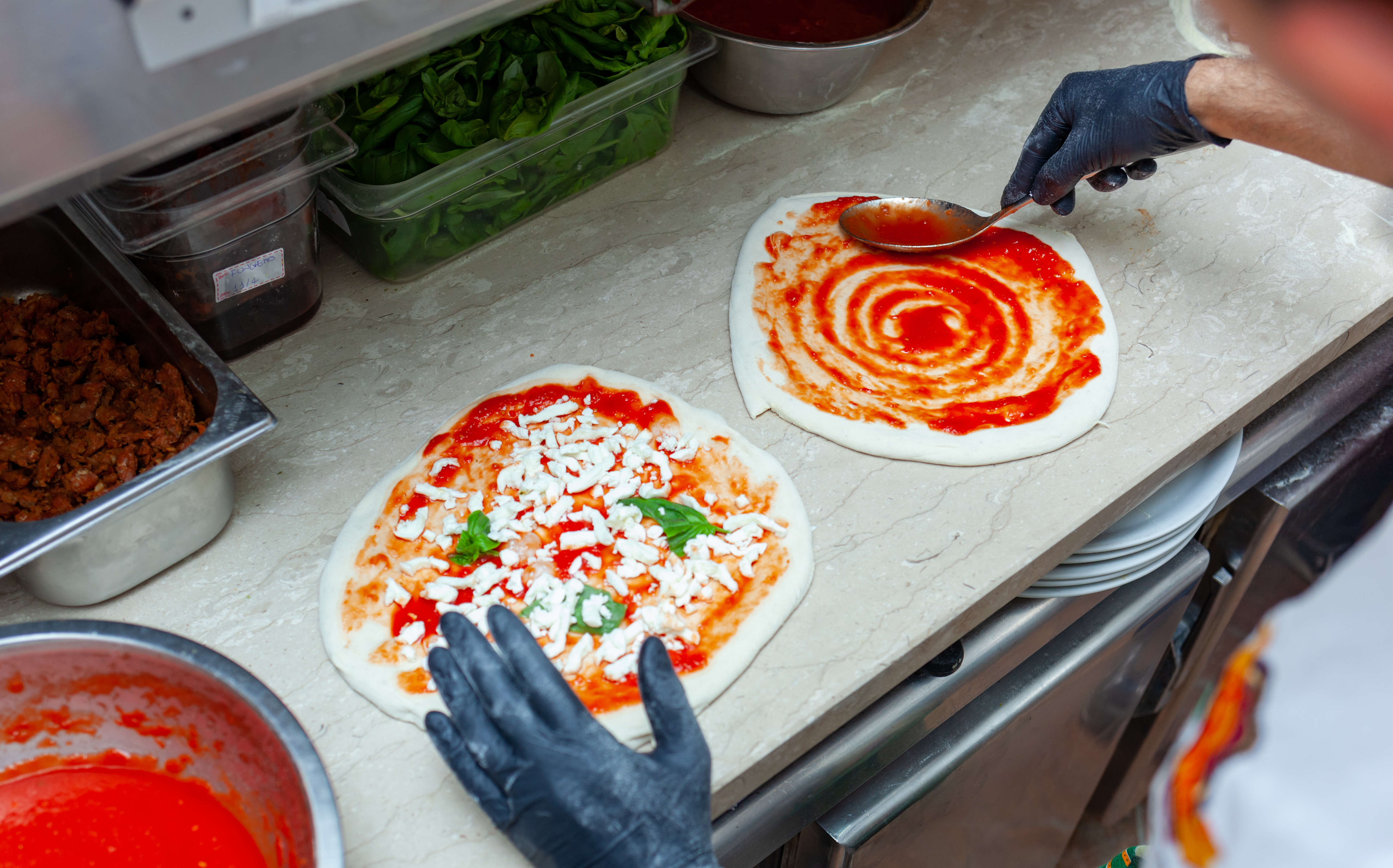 delicious pizza being topped with cheese and basil and sauce